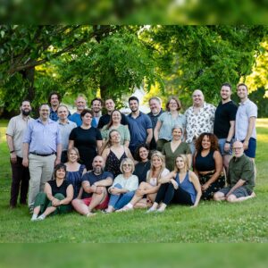 Vocal ensemble The Crossing posing outdoors in a green field in front of several trees.